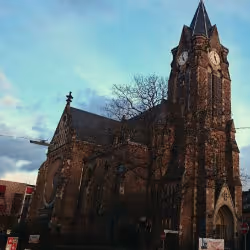 Historic stone church with a tall clock tower under a partly cloudy sky.