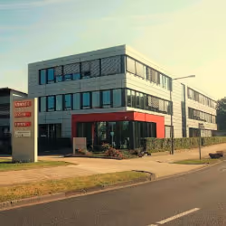 Modern commercial building with large windows and red accents next to a road under a clear sky.