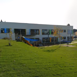 Modern, two-story building with blue-framed windows and a large grassy lawn in front under a clear sky.